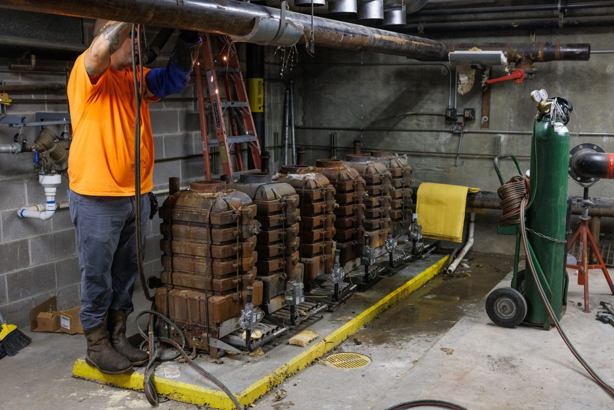 Worker cuts pipe next to iron boiler